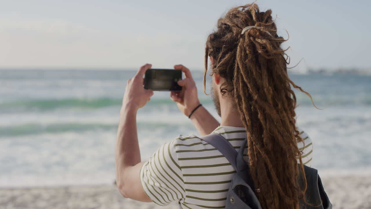 joven turista tomando fotos en la playa usando la tecnología de la cámara de su teléfono inteligente de un hermoso fondo panorámico del océano hombre caucásico disfrutando de las vacaciones de verano