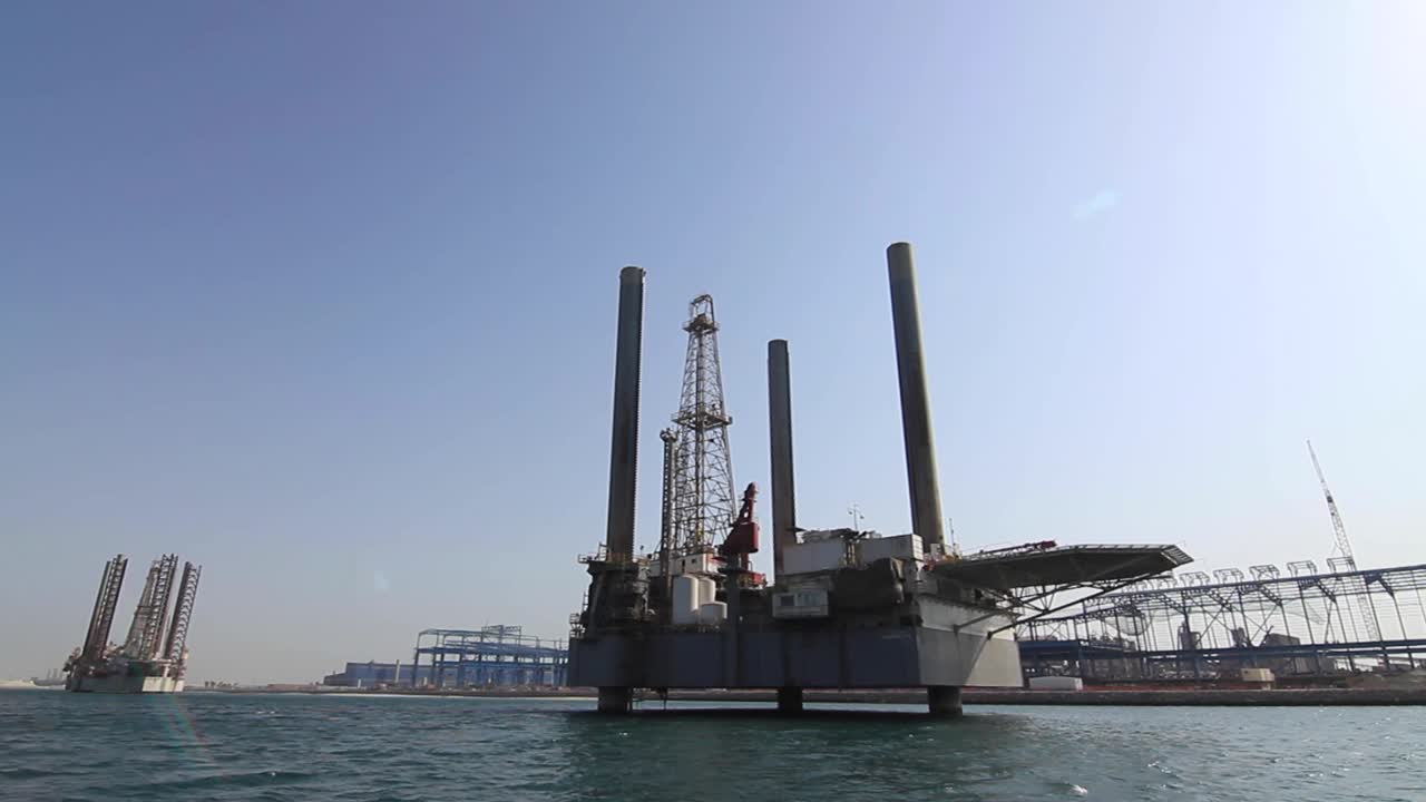 Moving shot from a boat of oil rigs close to port and dry dock awaiting repairs and re-deployment at sea in Bahrain in the Arabian Gulf