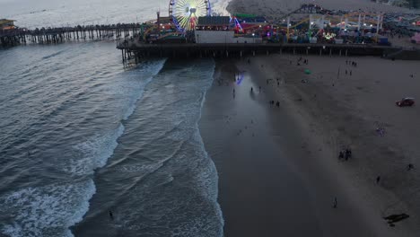 Aerial-reverse-pullback-tilting-up-shot-of-the-Santa-Monica-Pier-on-a-beautiful-summer-night-in-Los-Angeles,-California-at-twilight