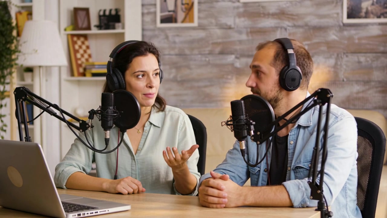 Grabando a una mujer con blusa verde y a un hombre con camisa vaquera hablando por micrófonos para un estudio de podcast.