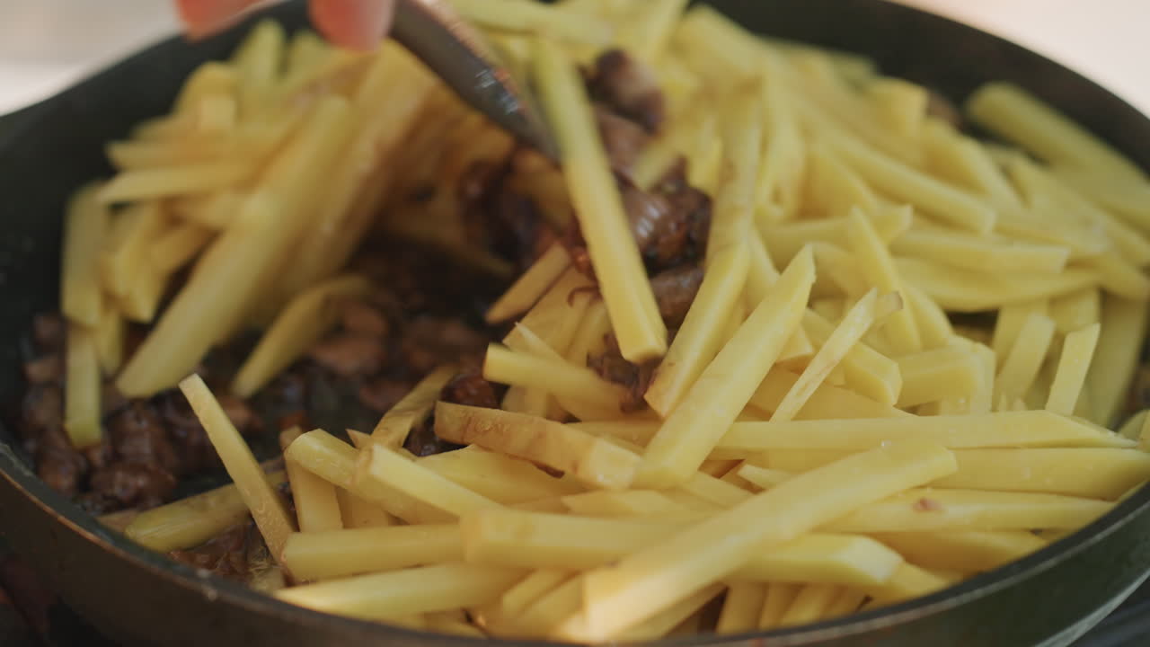Camping skillet meat fries closeup caucasian chef hands stir seared beef under golden fries, wooden spatula mixing juices, sizzling aroma, rustic campsite table at dusk, hearty outdoor meal, savory