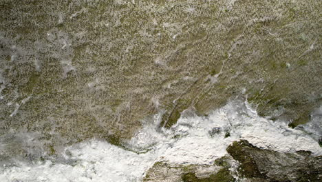 Top-down-aerial---rippling-water-hitting-the-shore---frothy-white-water---natural-environment