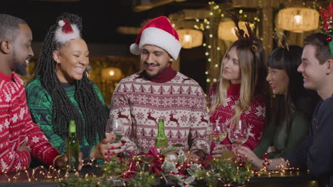 sliding shot of group of friends toasting drinks in bar during christmas celebrations