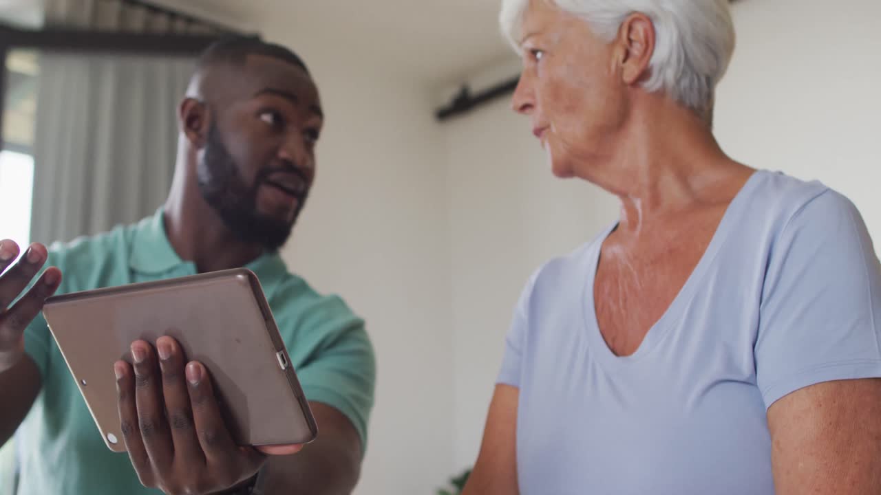 Video di fisioterapista maschio afroamericano che usa il tablet con anziana donna caucasica