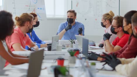 masked people sitting table in office. boss discussing team indoors.