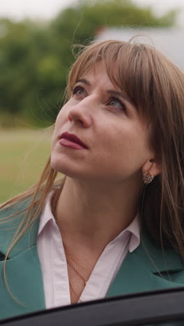 focused businesswoman stands near car looking at big building against vehicle passing by. long-haired lady closes door going away closeup slow motion