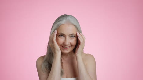 smiling senior woman demonstrating skincare on pink background