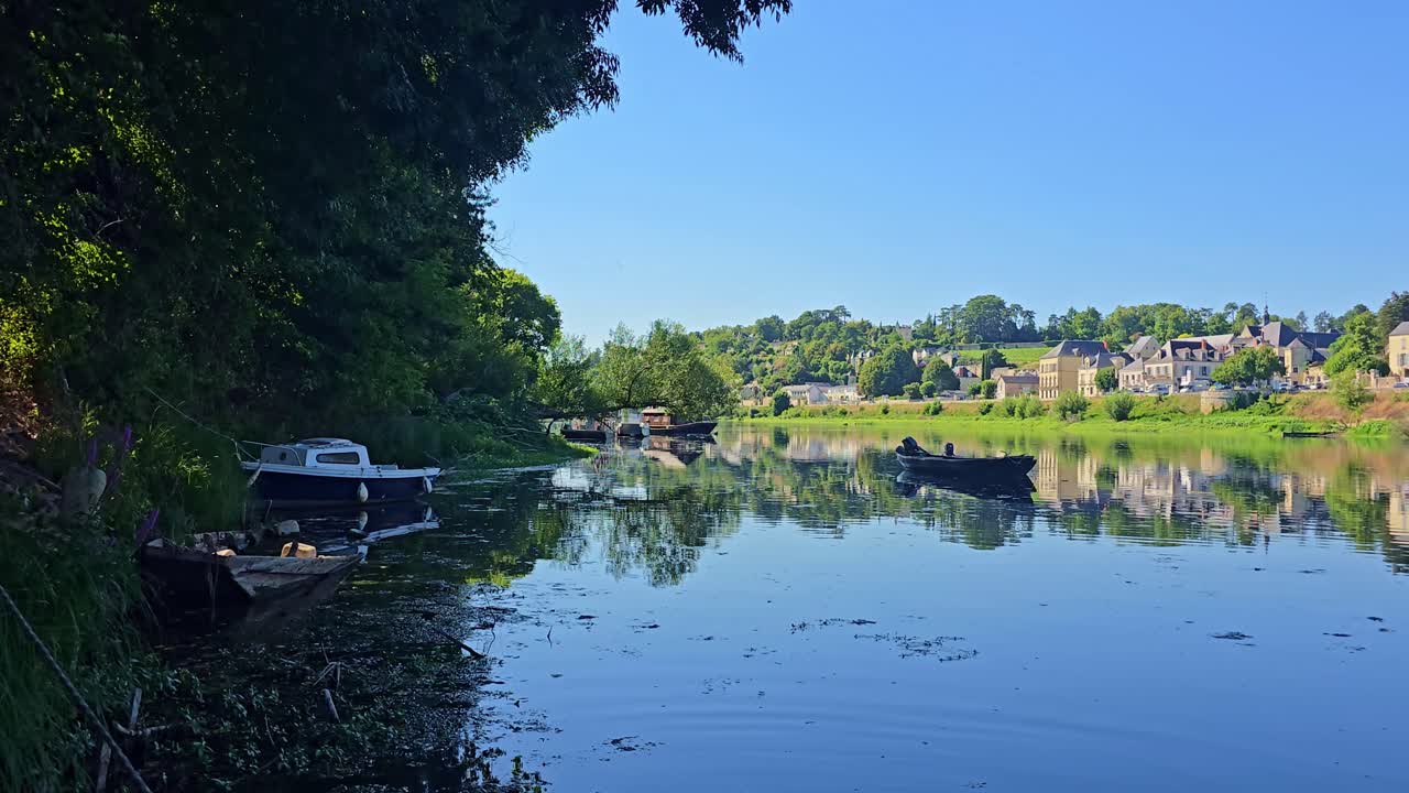 Static shot of boats in shade and light on Vienne River with Chinon houses beyond