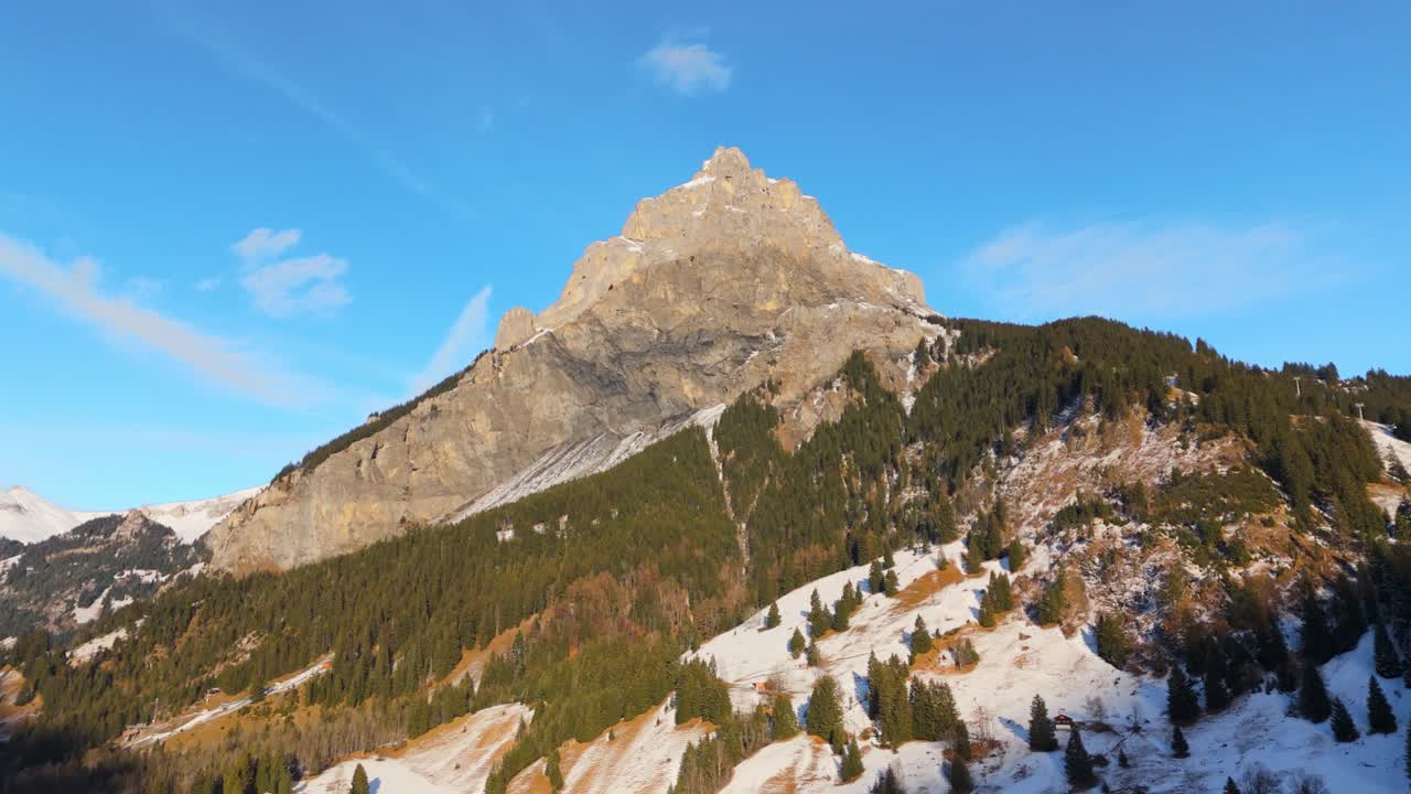 pico rocoso iluminado por el sol en las montañas de los alpes con la ladera de la montaña de bosque nevado