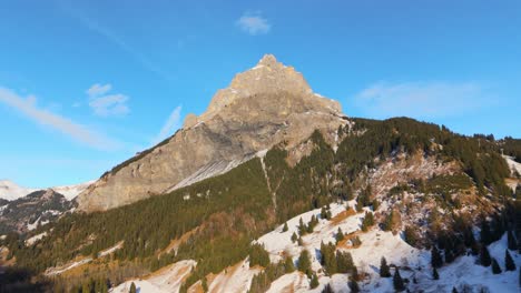 sunlit rocky peak in alps mountains with snowy forest mountainside