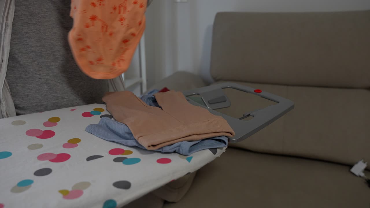 Pregnant woman carefully placing baby clothes on ironing board at home, 4K