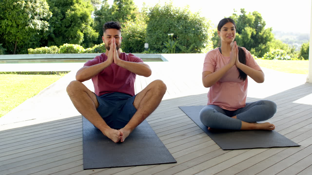 Couple practicing yoga outdoors on mats, smiling and enjoying relaxation