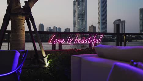 neon sign reading 'love is beautiful' against a skyline and river view for valentine day