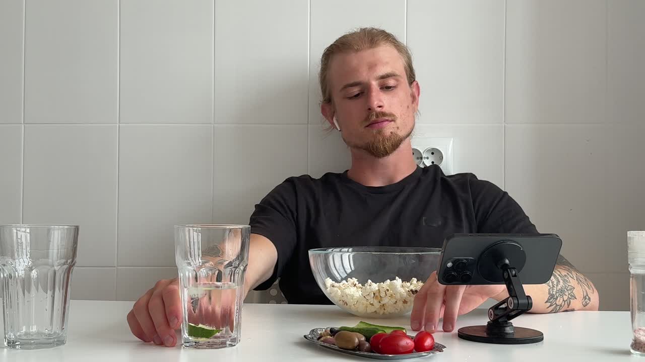 Mutfakta patlamış mısır yiyen ve telefona bakan genç adam