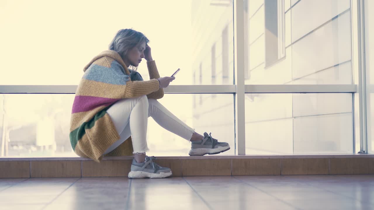 cámara lenta joven chica linda se sienta en el fondo de las ventanas pensativo