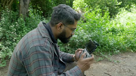 professional drone pilot using dji drone remote controller with a smartphone attached in a forest landscape for wildlife surveillance, india