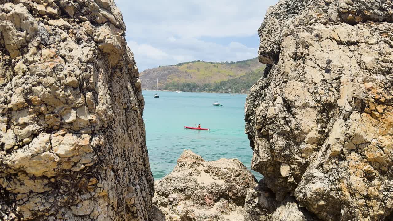 A kayaker navigates turquoise waters near rocky cliffs in Phuket, Thailand, under bright daylight, capturing a serene coastal scene