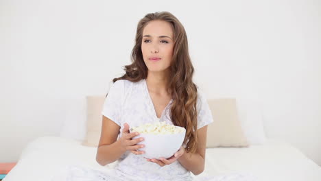 mujer joven comiendo un plato de palomitas de maíz en la cama