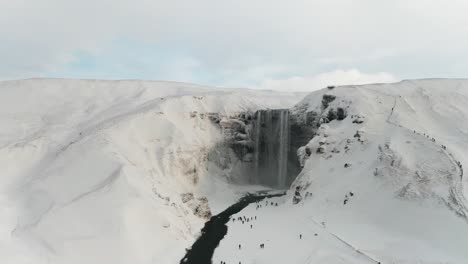 a beautiful large waterfall in iceland in mid-winter covered by the snow around it and the clouds makes it even better