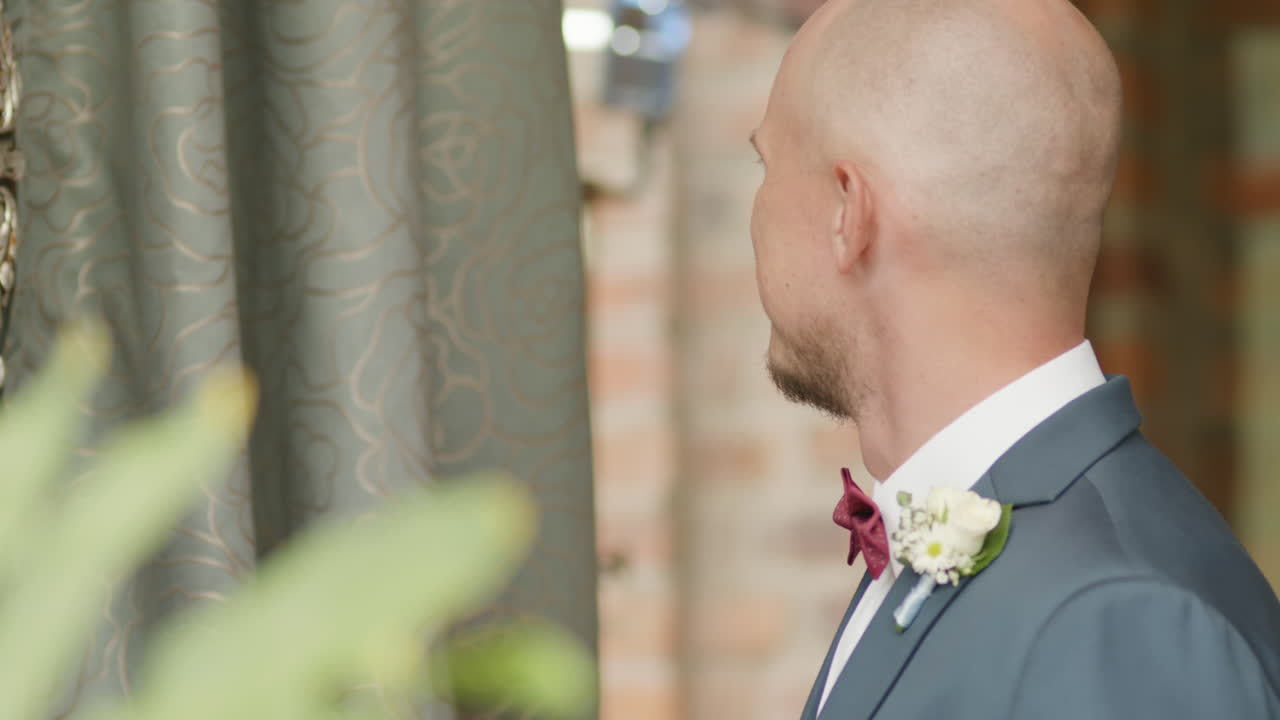Clip of a groom looking in the mirror while adjusting his bow tie, preparing for the big day.