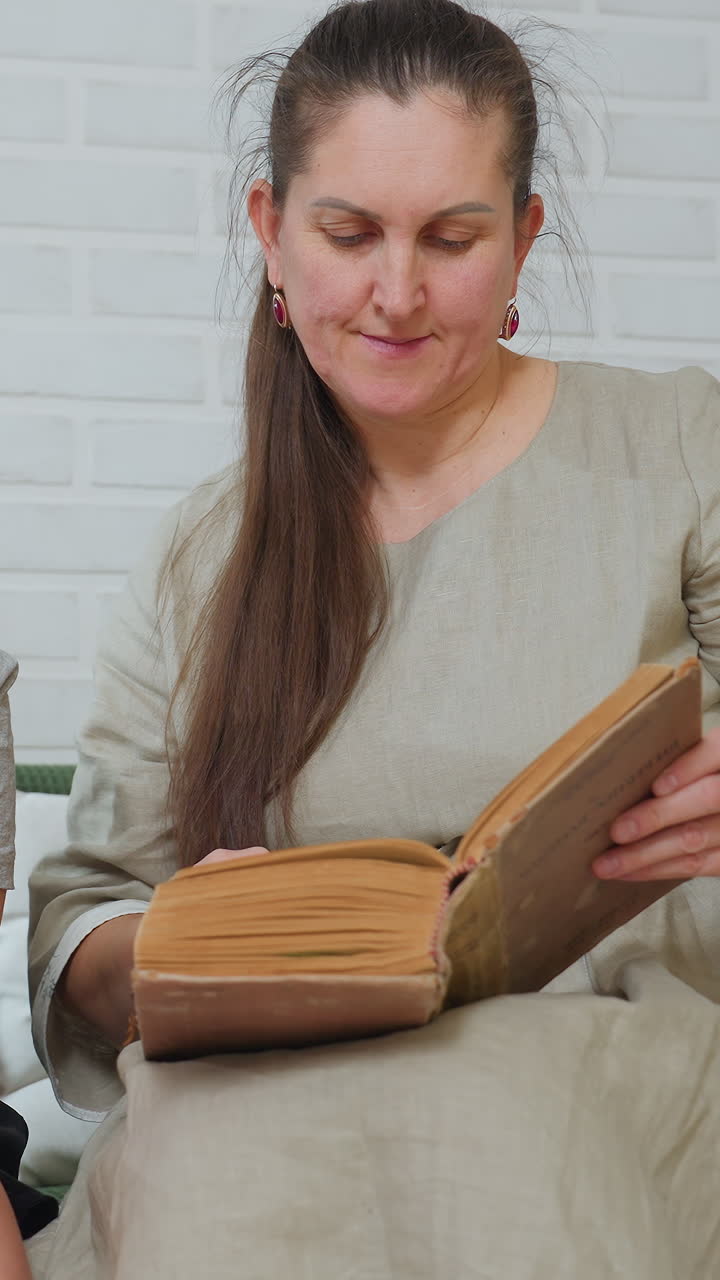 Mujer caucásica leyendo un libro antiguo con un vestido de lino beige, sentada junto a una pared de ladrillo blanco, hojeando páginas amarillentas; un momento de calma y soledad que se transforma cuando se convierte en una amable tutora, señalando el texto