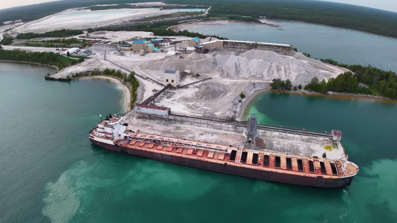 Aerial view of large cargo ship docked at industrial port facility with surrounding turquoise waters