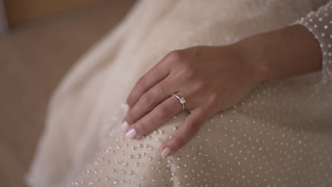 close-up of a bride's hand resting on a beaded wedding dress, showing a diamond engagement ring