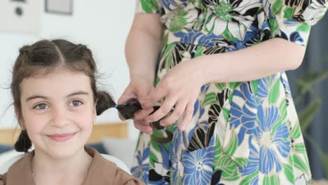 a person styling a young girl's hair into pigtails