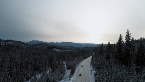 Viaje-Por-Carretera-En-El-País-De-Las-Maravillas-Invernal:-Una-Toma-Escénica-De-Los-Autos-En-La-Carretera-24-Del-Pequeño-Fuerte-Cubierto-De-Nieve,-Rodeada-De-Bosques-Y-Montañas-A-La-Luz-De-La-Hora-Dorada