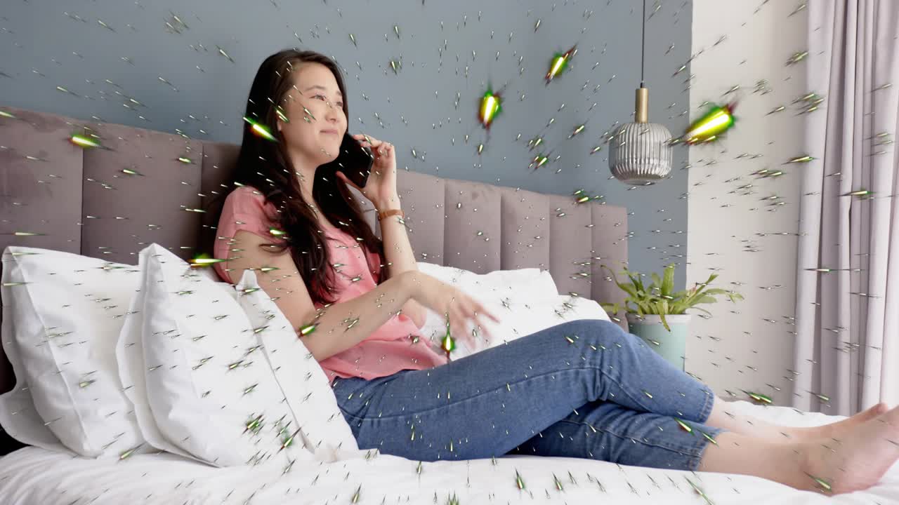 Woman reclining on bed using phone, holding to ear for social call; green particles overlaying tech