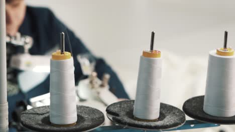 primer plano de una máquina de coser que desenrolla hilos blancos para coser en una fábrica textil