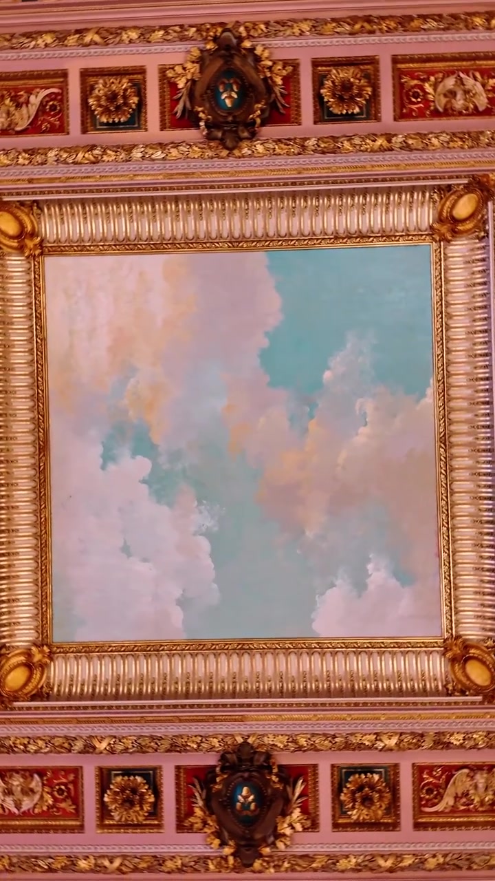 Pittura ornamentale sul soffitto di nuvole con modanature decorative dorate. Vista interna di un soffitto classico caratterizzato da un murale del cielo circondato da elaborate cornici e pannelli dorati.