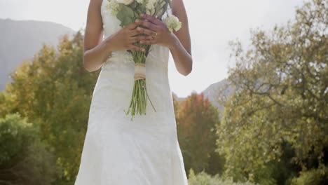 Feliz-Novia-Afroamericana-Caminando-Sosteniendo-Ramo-En-Su-Boda-En-Un-Jardín-Soleado,-Cámara-Lenta