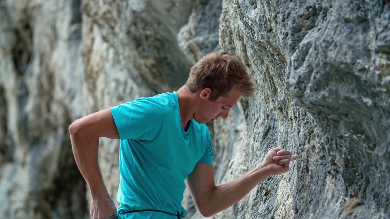 Young handsome man rock climber stands, looks up and chalks hands, close up