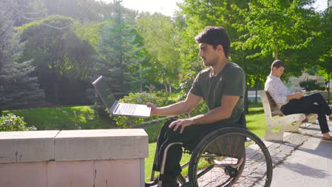 teenager sitting in wheelchair working with laptop outdoors.