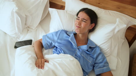 woman in blue pajamas waking up in bed with smartphone nearby, at home