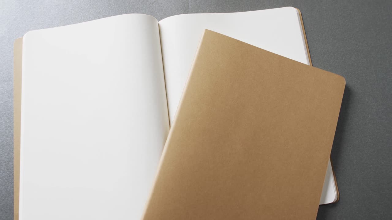 Close up of open blank book and brown notebook with copy space on gray background in slow motion