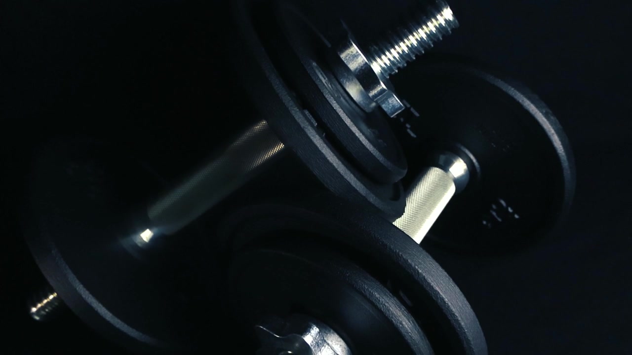 Manubrio in acciaio con dischi di peso intercambiabili appoggiato su uno sfondo scuro, che rappresenta attrezzatura da palestra per bodybuilding, allenamenti fitness ed esercizio fisico intenso in un ambiente di palestra professionale.