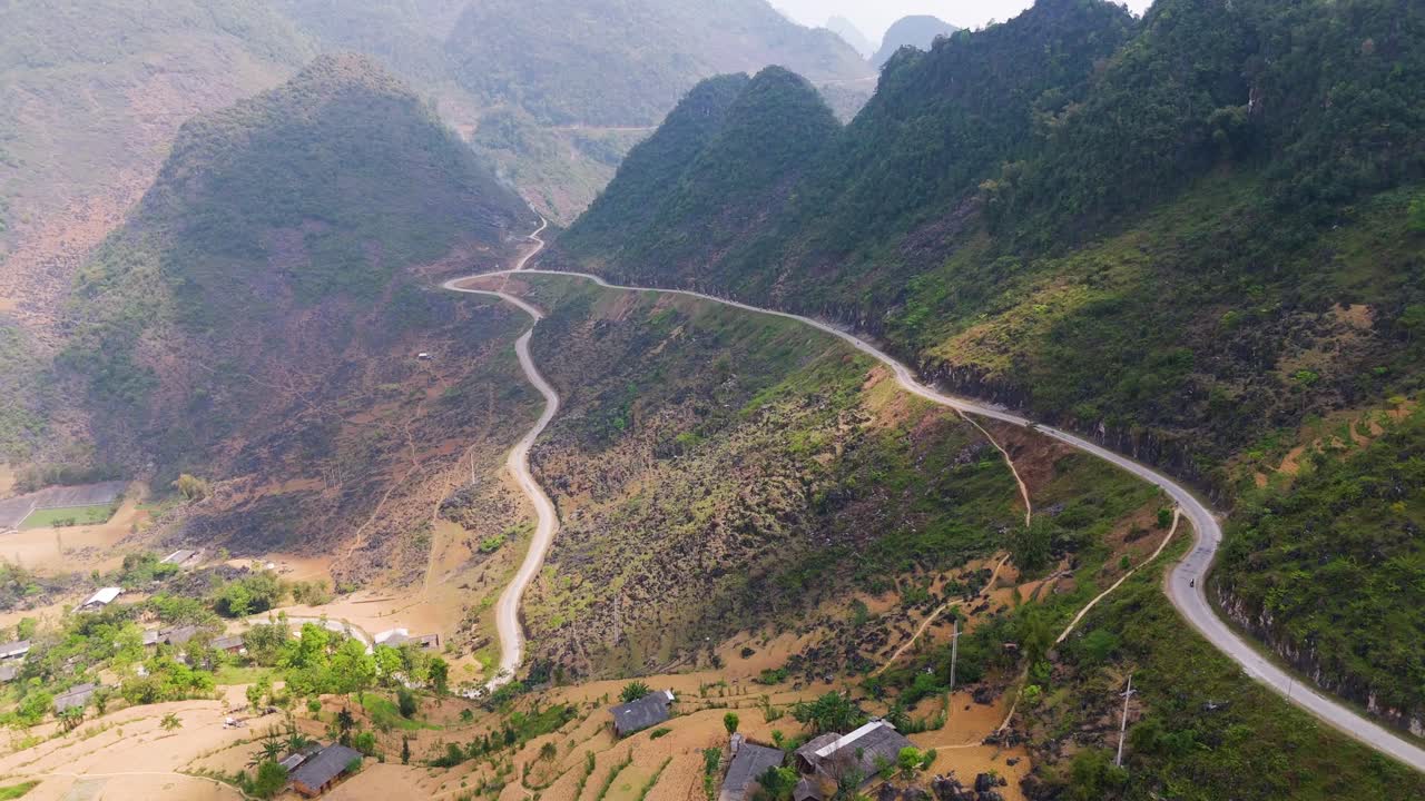 A thrilling aerial view of Ha Giang's serpentine roads, teeming with motorcycles winding through lush rice fields and towering mountains.