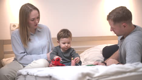 vista lejana de un bebé jugando con un juguete en la cama con sus padres