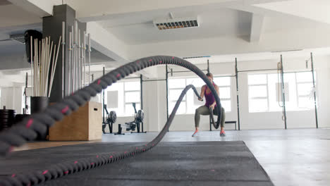 mujer biracial inalterada concentrada haciendo ejercicio con cuerdas de lucha en el gimnasio, en cámara lenta