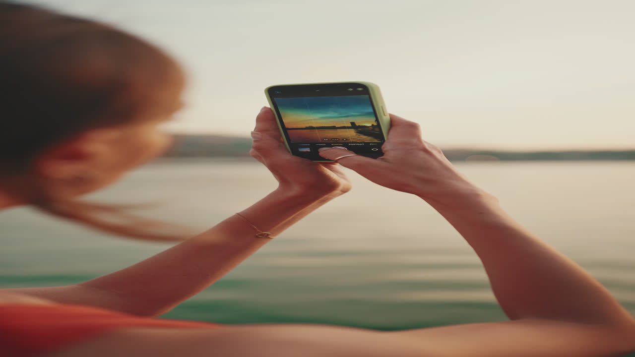 Woman taking a photo of sunset with smartphone