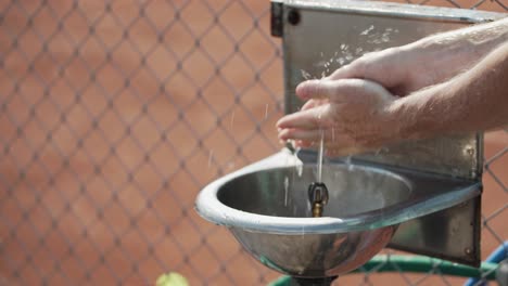 primer plano en cámara lenta de un hombre lavándose las manos en un fregadero de acero inoxidable con agua que salta del grifo