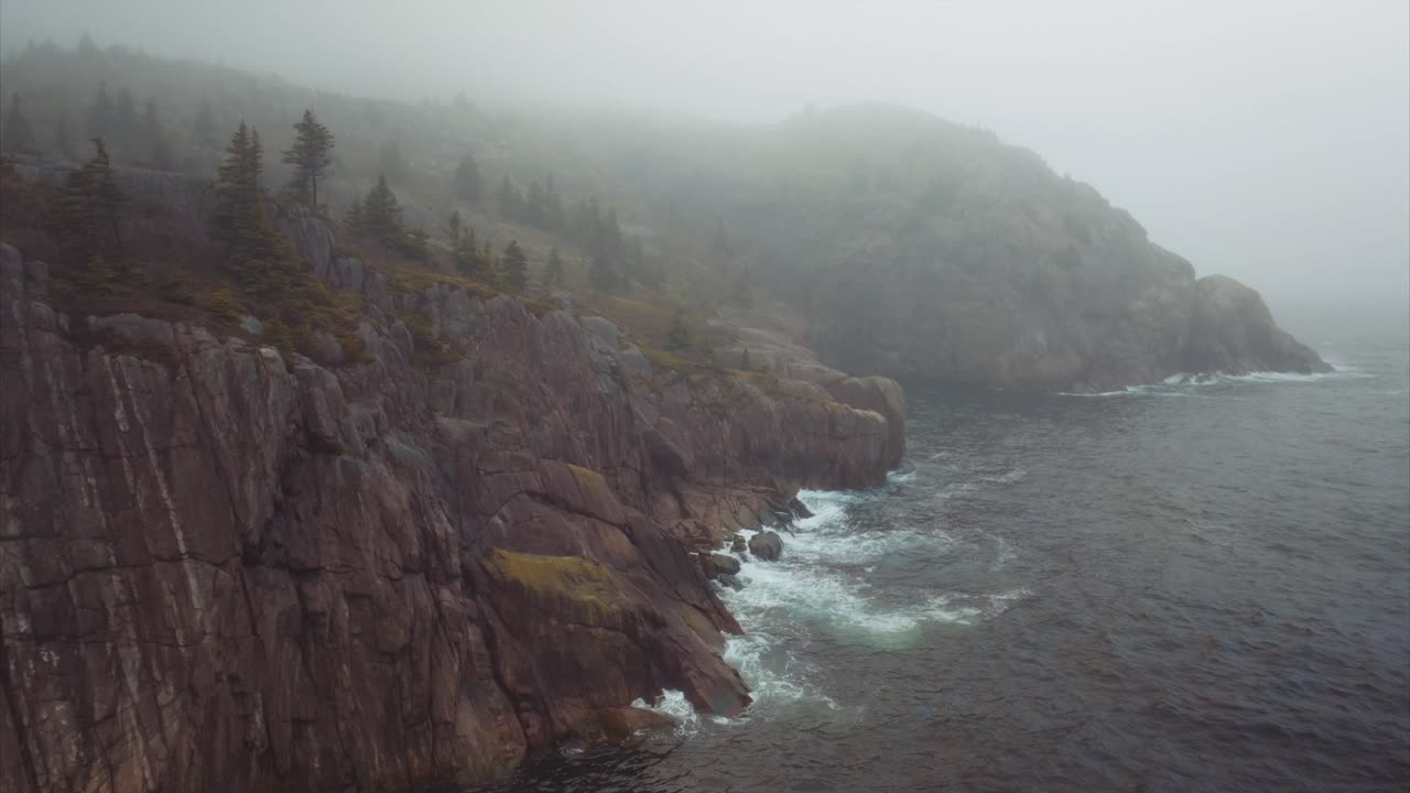Fog hangs on sparse landscape with rocky cliffs descending to the sea far below