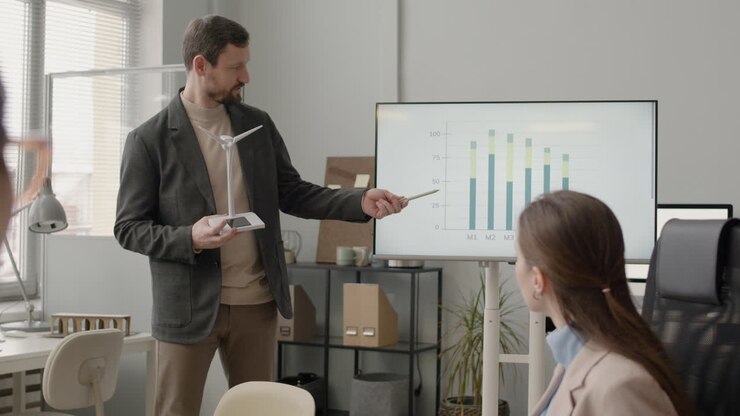 Empresario explicando un modelo de aerogenerador y mostrando un gráfico de datos durante una reunión en la oficina