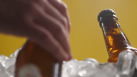 cerrar las botellas de vidrio de cerveza fría o refrescos que se enfrían en un cubo lleno de hielo contra un fondo amarillo 1