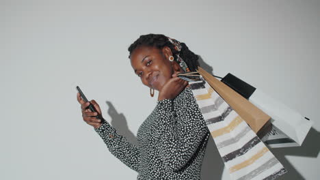 beautiful african american woman posing in studio with shopping bags and phone