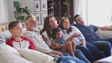 three generation hispanic family sitting on the sofa watching tv, grandmother using remote control