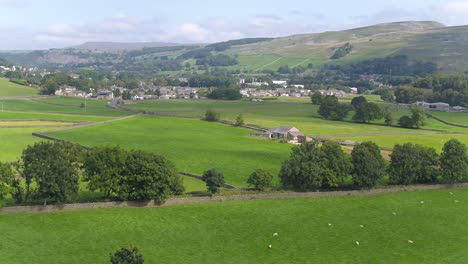 Drohnenaufnahmen,-Die-Sich-Seitwärts-Bewegen-Und-über-Ackerland-Und-Felder-In-Der-Nähe-Des-Ländlichen-Dorfes-Settle,-Yorkshire,-Großbritannien,-Mit-Schafen,-Trockenmauern,-Bäumen-Mit-Häusern-Und-Einer-Hügeligen-Landschaft-Schwenken