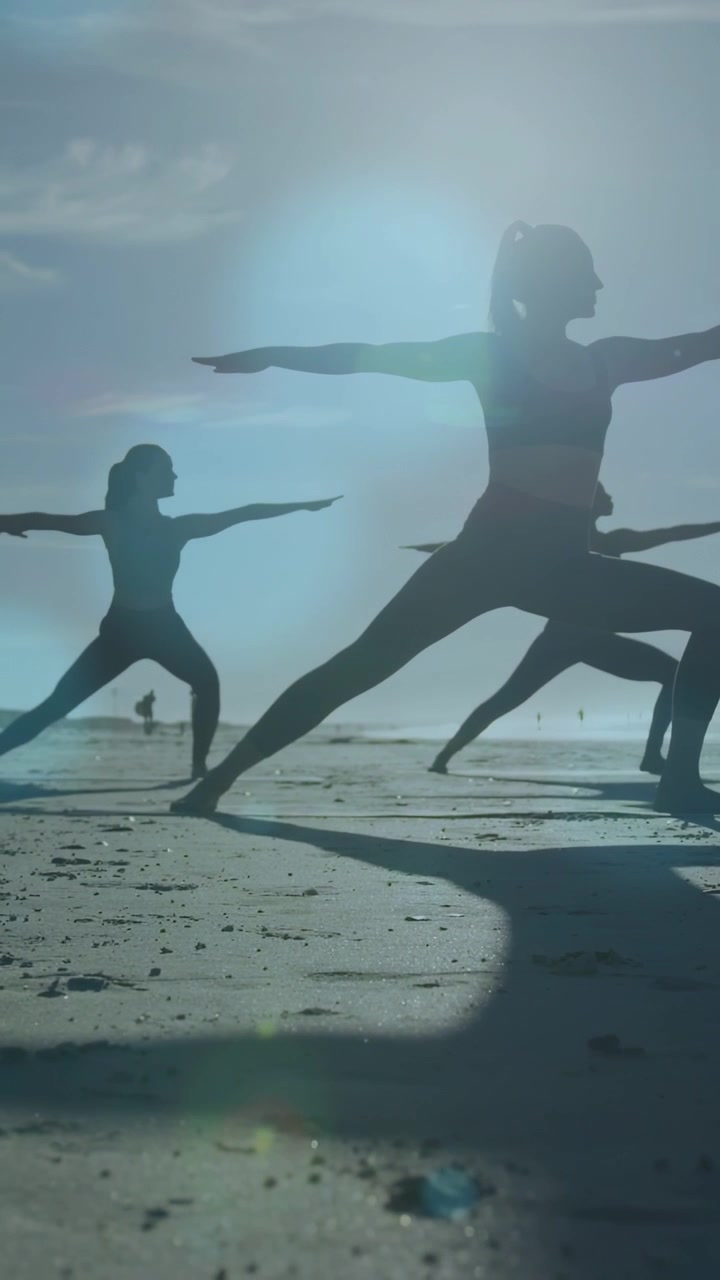 Vertical video: Lead woman stepping into wide stance, holding Warrior pose for fitness, sun flaring